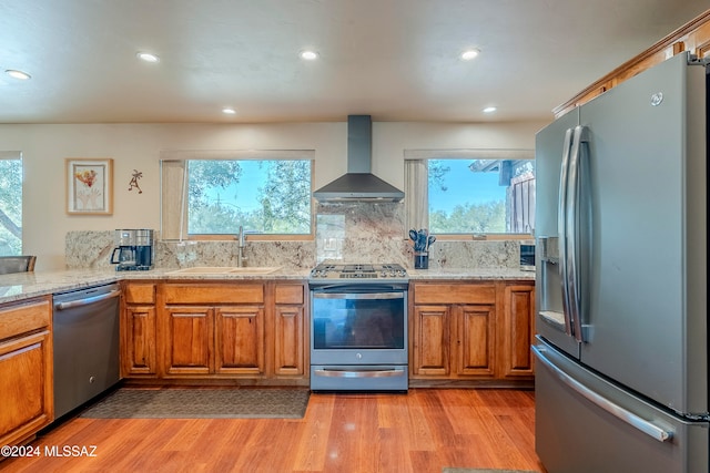 kitchen featuring wall chimney exhaust hood, light hardwood / wood-style floors, a wealth of natural light, and appliances with stainless steel finishes