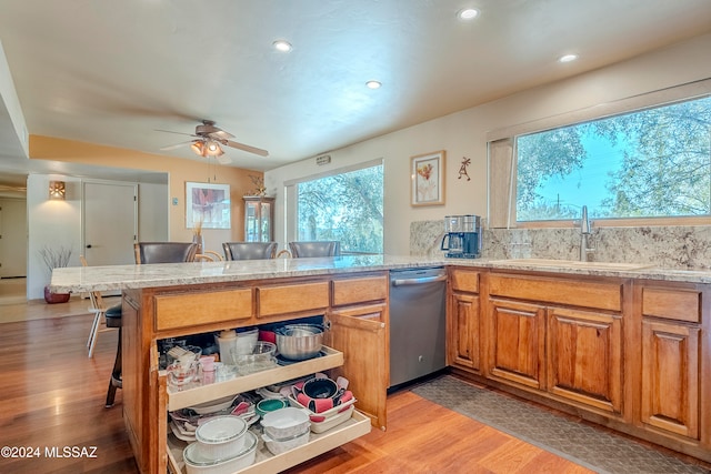 kitchen with a kitchen bar, kitchen peninsula, stainless steel dishwasher, sink, and light hardwood / wood-style floors