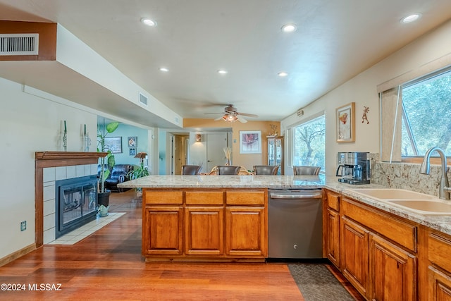 kitchen with kitchen peninsula, light wood-type flooring, stainless steel dishwasher, ceiling fan, and sink