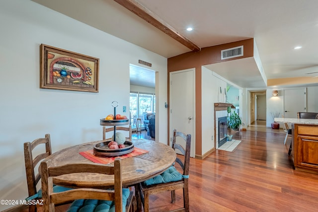 dining space featuring a fireplace, ceiling fan, light hardwood / wood-style flooring, and beamed ceiling