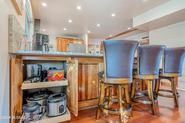 bar with light brown cabinets, light wood-type flooring, and stainless steel refrigerator