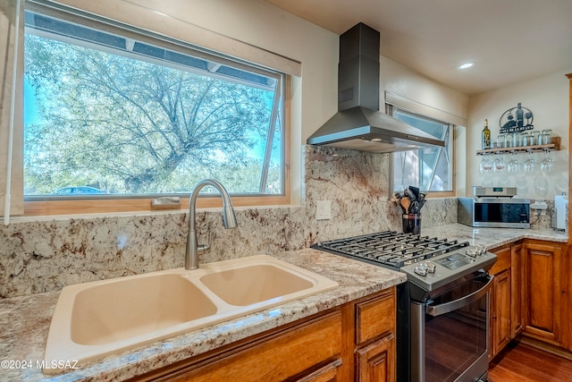 kitchen with hardwood / wood-style floors, wall chimney range hood, sink, appliances with stainless steel finishes, and tasteful backsplash