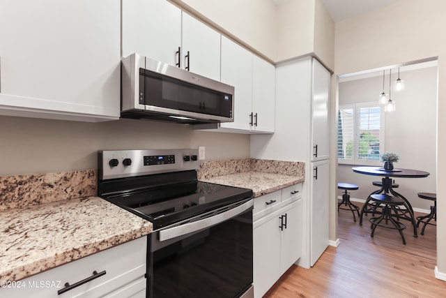 kitchen with light stone countertops, light wood-type flooring, stainless steel appliances, decorative light fixtures, and white cabinets