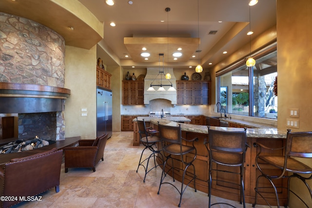 kitchen featuring kitchen peninsula, high end refrigerator, light stone countertops, tasteful backsplash, and hanging light fixtures