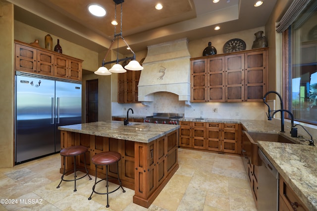 kitchen featuring pendant lighting, a center island with sink, a raised ceiling, decorative backsplash, and stainless steel appliances