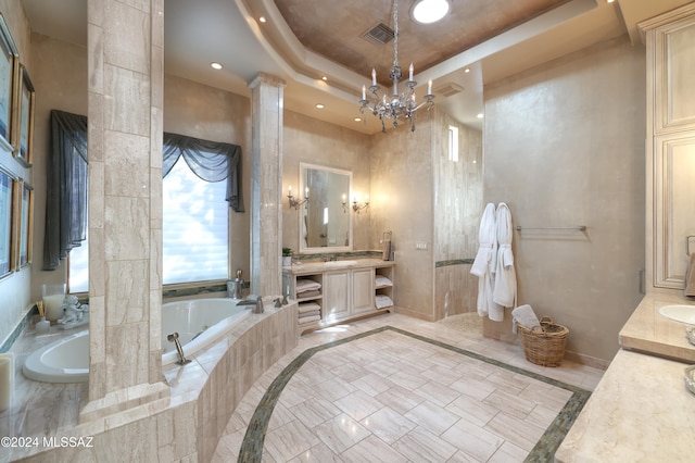 bathroom featuring an inviting chandelier, decorative columns, tiled tub, a tray ceiling, and vanity