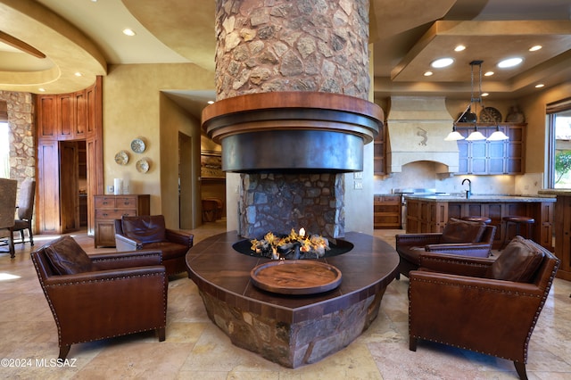 living room featuring a tray ceiling, a stone fireplace, and sink