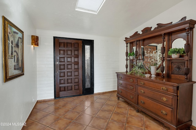 entryway featuring tile patterned floors, brick wall, and lofted ceiling