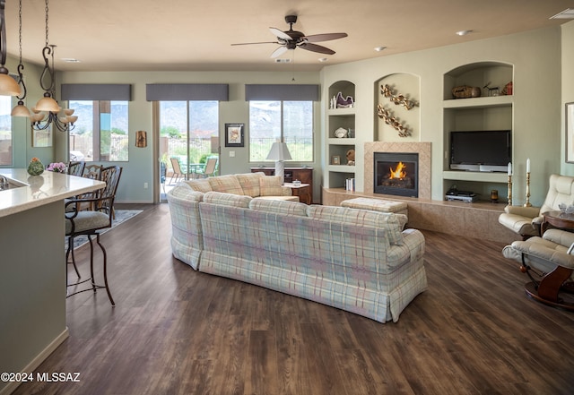 living room featuring dark hardwood / wood-style floors, built in features, a healthy amount of sunlight, and a tiled fireplace