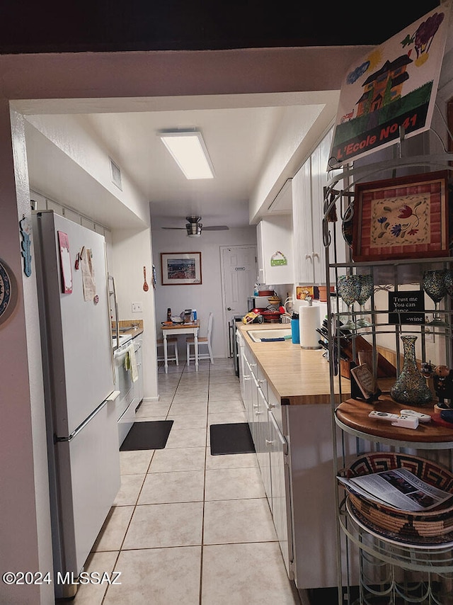 kitchen with stainless steel range, light tile patterned floors, white fridge, white cabinetry, and butcher block counters