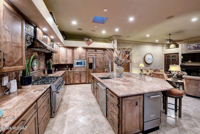 kitchen with a kitchen bar, crown molding, stainless steel appliances, light stone countertops, and a kitchen island with sink