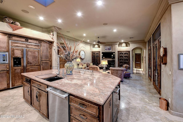 kitchen with sink, built in appliances, a kitchen breakfast bar, ceiling fan, and a kitchen island with sink