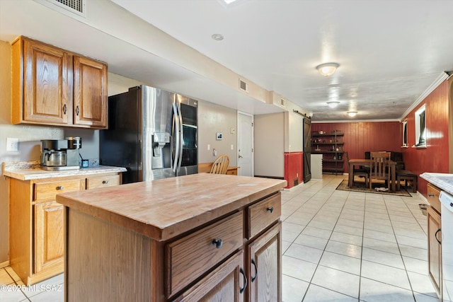 kitchen featuring stainless steel fridge, a barn door, wood walls, a kitchen island, and light tile patterned flooring