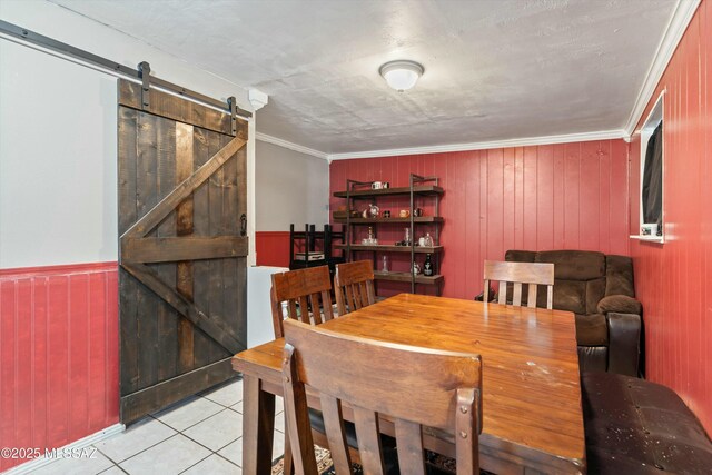 dining space with crown molding, wooden walls, a barn door, light tile patterned floors, and a textured ceiling