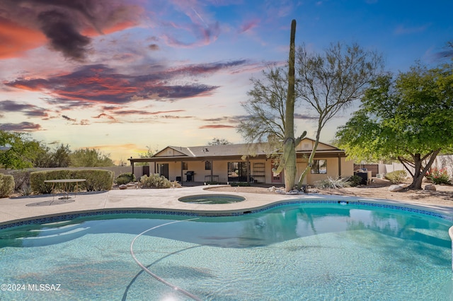 pool at dusk with an in ground hot tub and a patio