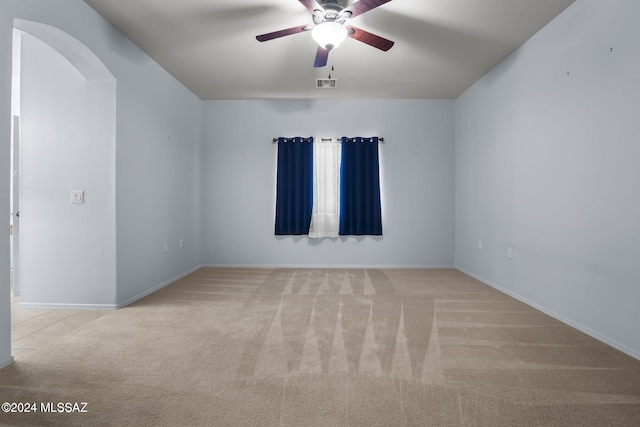 carpeted empty room featuring arched walkways, ceiling fan, visible vents, and baseboards