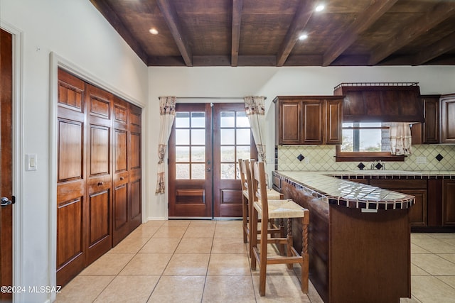 kitchen with beam ceiling, tile counters, tasteful backsplash, a breakfast bar area, and wood ceiling