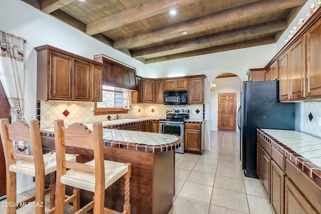 kitchen featuring beam ceiling, tasteful backsplash, tile counters, and black appliances