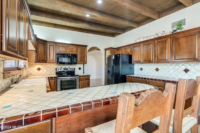 kitchen featuring tile counters, sink, beamed ceiling, backsplash, and black appliances