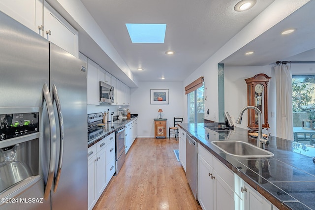 kitchen featuring sink, light wood-type flooring, a skylight, appliances with stainless steel finishes, and white cabinets