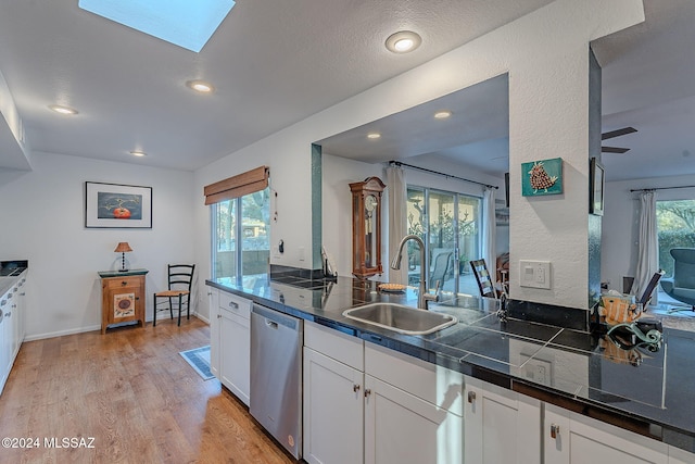 kitchen with sink, white cabinets, stainless steel dishwasher, and a skylight