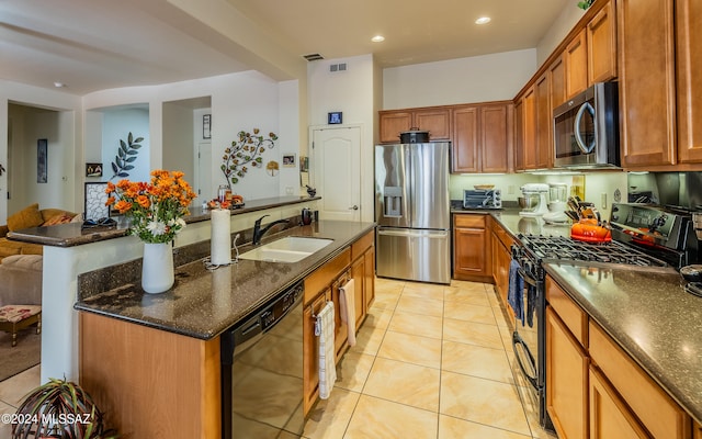 kitchen with a center island with sink, visible vents, brown cabinetry, appliances with stainless steel finishes, and a sink