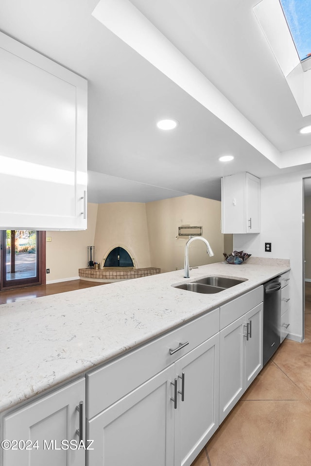 kitchen featuring kitchen peninsula, light stone counters, stainless steel dishwasher, sink, and white cabinetry