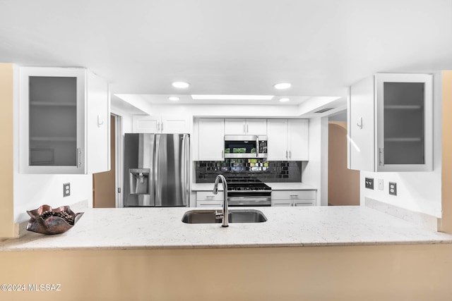 kitchen with light stone countertops, decorative backsplash, stainless steel appliances, sink, and white cabinetry