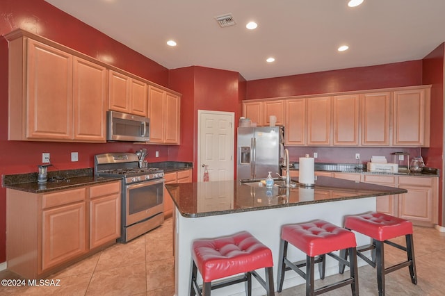 kitchen featuring appliances with stainless steel finishes, a kitchen bar, dark stone countertops, a center island with sink, and recessed lighting