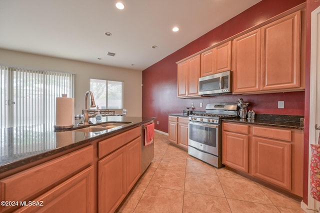kitchen with stainless steel appliances, a sink, dark stone countertops, light tile patterned flooring, and recessed lighting