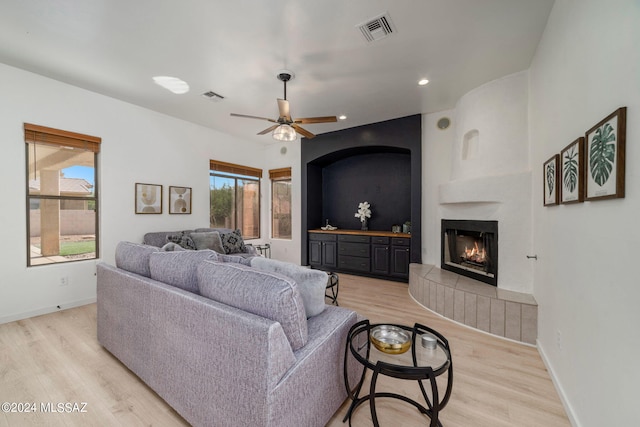 living room featuring ceiling fan, a fireplace, and light hardwood / wood-style flooring