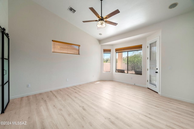 unfurnished room with a barn door, ceiling fan, light hardwood / wood-style flooring, and vaulted ceiling