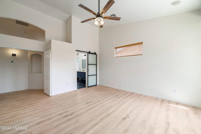 empty room featuring ceiling fan, a barn door, light hardwood / wood-style floors, and a high ceiling