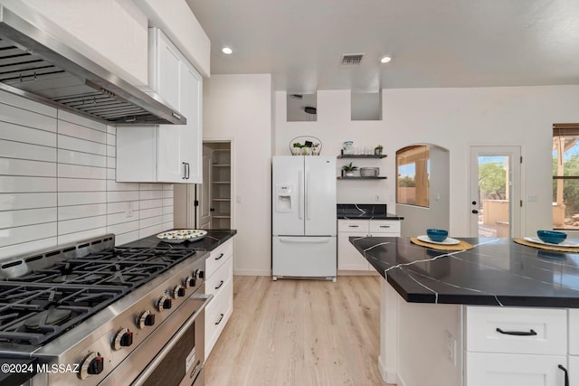 kitchen with white fridge with ice dispenser, a center island, wall chimney range hood, high end stainless steel range oven, and white cabinets