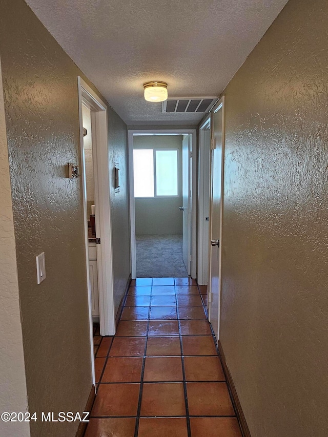 hall with a textured ceiling and dark tile patterned floors