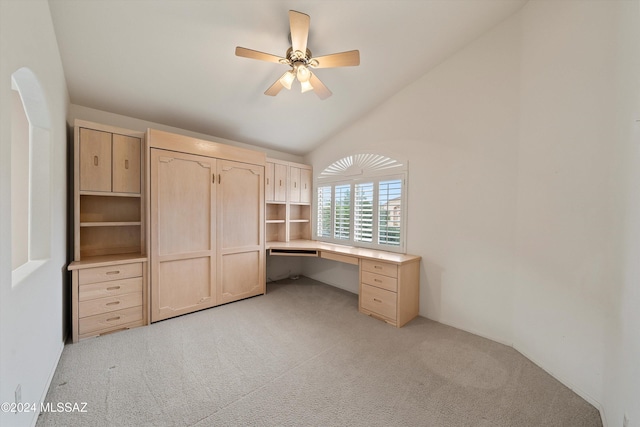 unfurnished office featuring ceiling fan, light colored carpet, built in desk, and vaulted ceiling