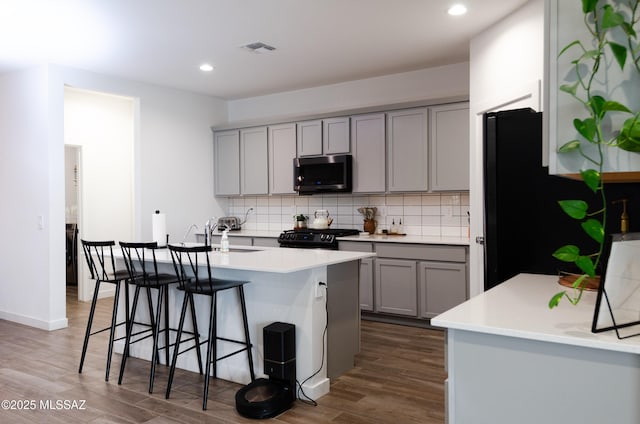 kitchen with gray cabinetry, a kitchen island with sink, sink, dark hardwood / wood-style flooring, and a breakfast bar area