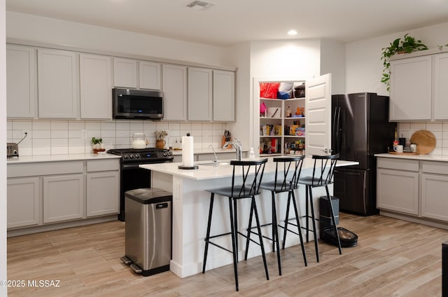 kitchen with freestanding refrigerator, a sink, light wood-style floors, range with gas cooktop, and stainless steel microwave