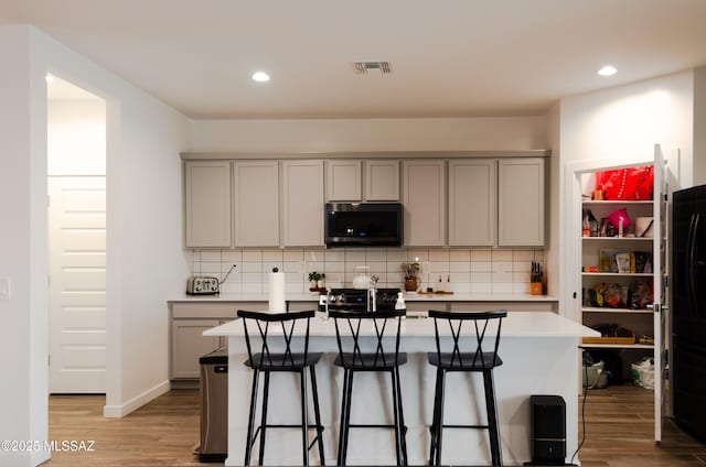 kitchen featuring light wood-style floors, stainless steel microwave, tasteful backsplash, and gray cabinets