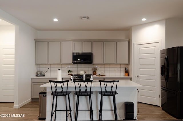 kitchen with stainless steel microwave, black fridge, gray cabinets, and visible vents