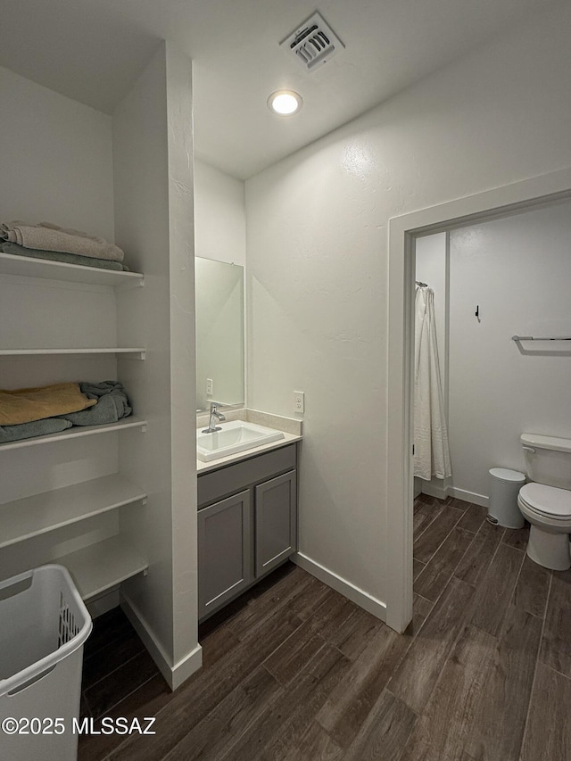 bathroom with vanity, wood finished floors, visible vents, baseboards, and toilet