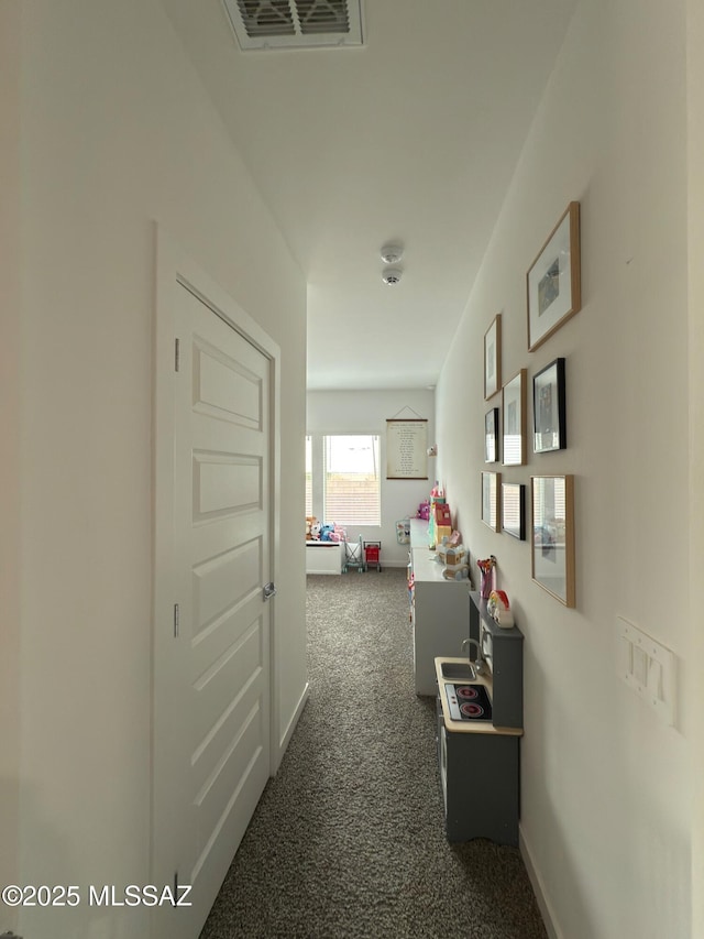 hallway with baseboards, visible vents, and dark colored carpet