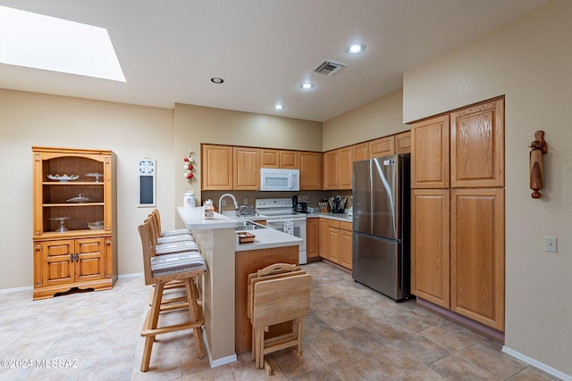 kitchen featuring a skylight, sink, kitchen peninsula, white appliances, and a breakfast bar