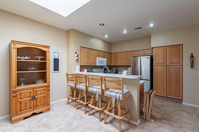 kitchen with a kitchen bar, kitchen peninsula, stainless steel refrigerator, and range