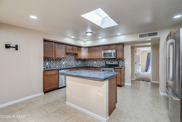 kitchen with a skylight, stainless steel appliances, light tile patterned floors, tasteful backsplash, and a kitchen island