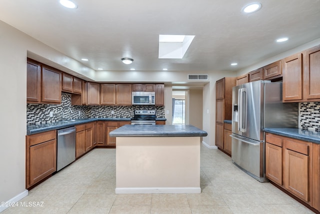 kitchen with a skylight, light tile patterned floors, tasteful backsplash, a kitchen island, and stainless steel appliances