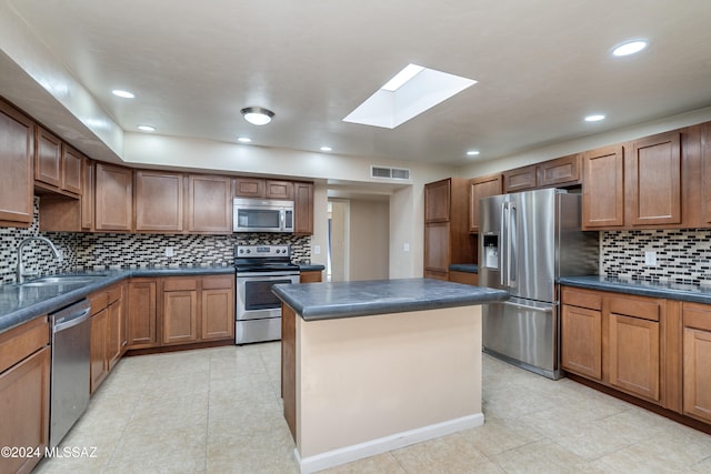 kitchen with decorative backsplash, a skylight, stainless steel appliances, sink, and a center island