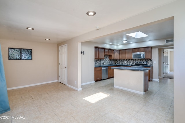 kitchen with a skylight, light tile patterned floors, decorative backsplash, a kitchen island, and appliances with stainless steel finishes