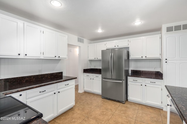 kitchen with stainless steel fridge, dark stone countertops, white cabinetry, and light tile patterned floors