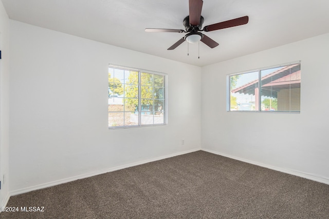 empty room featuring a wealth of natural light, ceiling fan, and dark carpet